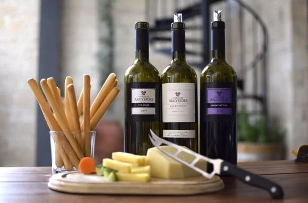 Tres botellas de vino con una tabla de queso, un cuchillo y pan dentro de un vaso.