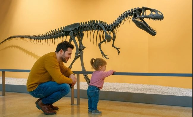 Padre con su hija pequeña en el museo de Ciencias Naturales de Valencia mirando un esqueleto de dinosaurio