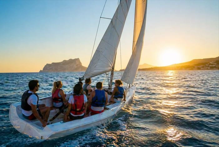 Grupo de personas navegando en un barco de vela ligera al atardecer frente a la costa de Moraira (Alicante), disfrutando del mar y las vistas de la Costa Blanca.