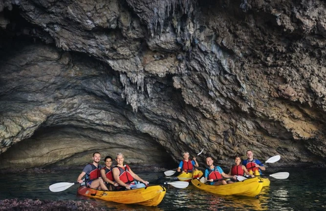 Grupo de turistas navegando en kayak dentro de una cueva marina en la Cala Granadella, Jávea, rodeados de formaciones rocosas y aguas tranquilas durante una excursión guiada.