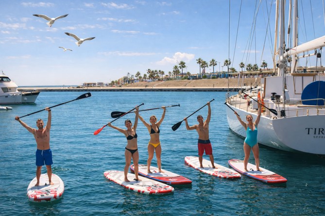 Grupo de personas haciendo paddle surf en Valencia en la playa de la Malvarrosa con mar tranquilo y gaviotas volando